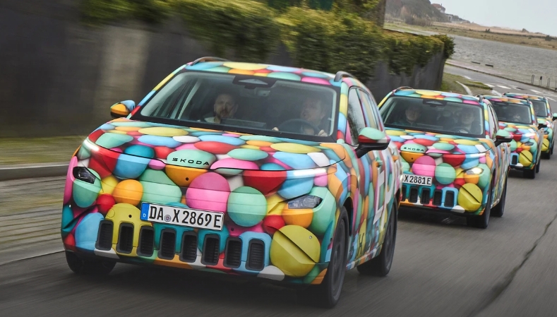 mehrere bunt beklebte Skoda Epiq hintereinander auf einer Straße